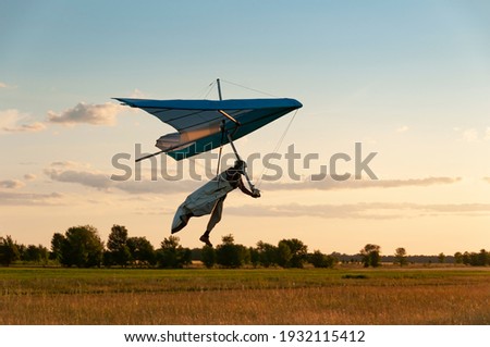 Learning to fly on a hang glider. Pilot prepares to land with his wing. Hang glider wing silhouette