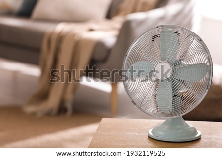 Modern electric fan on wooden table in living room. Space for text Royalty-Free Stock Photo #1932119525