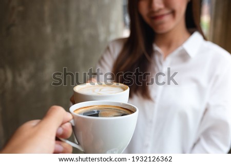 Closeup image of woman and a man clink white coffee mugs in cafe