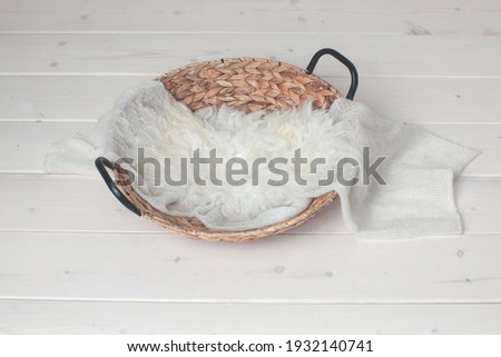 Wicker basket on a wooden background. Photo zone for taking pictures of a newborn baby. White fur, winding. Preparing for a photo session. Photoshoot. Props. Newborn nest. 