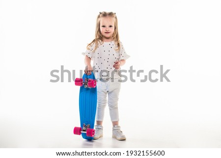 Charming active school girl in fashionable trendy outfit, playful and smiley, showing v symbol, with toothy smile, skate in hands, amazing wavy hairdo