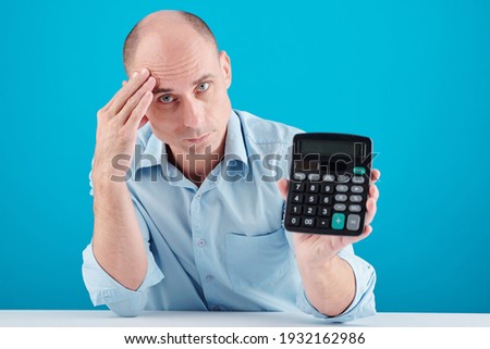 Tired stressed frowning mature bald man showing calculator, personal finances concept
