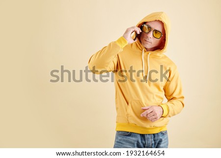 Studio portrait of man in yellow hoodie and sunglasses talking on phone with friend