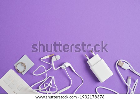 a set of accessories for a smartphone, charger, headphones, holding a ring, adapters for sim cards on a purple background copy space top view