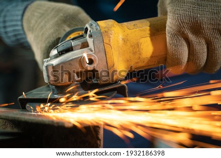 Locksmith in special clothes and goggles works in production. Metal processing with angle grinder. Sparks in metalworking.