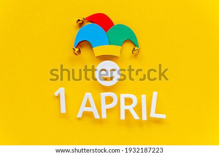 April fools day over yellow background with jester hat. First April card with laughing face. Copy space for text, top view.  