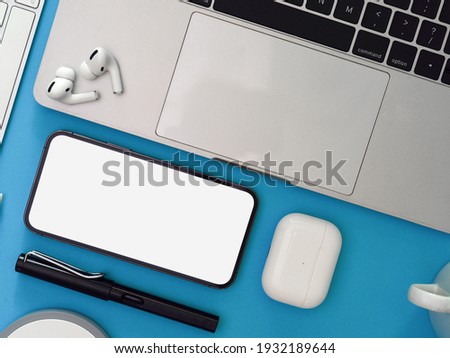 Creative flat lay workspace with smartphone, laptop, earphone and supplies on light blue background, clipping path, top view