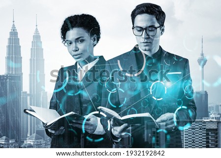 Two colleagues in multinational corporate team working on technology at business process to achieve tremendous growth in commerce. Tech hologram icons over Kuala Lumpur background
