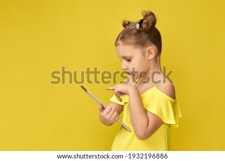 funny little child girl in yellow t-shirt using digital tablet on yellow background