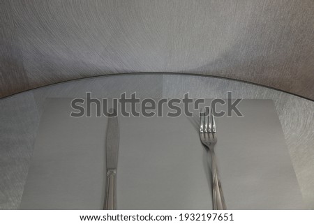 The knife on the left and the fork on the right are served on a gray napkin in close-up.Monochrome image.Grey background.Concept silver cutlery of everyday life