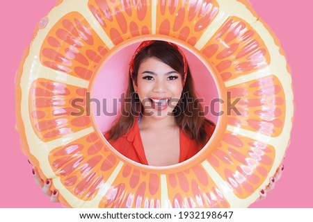 Portrait beautiful woman holding orange inflatable round standing over pink background