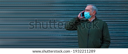 adult man with medical mask talking with mobile phone on gray blind background