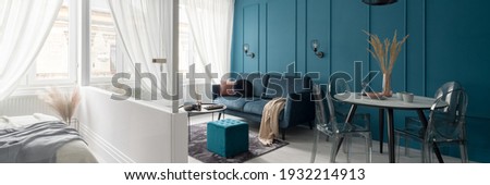 Panorama of elegant and small living room with dining area ane with teal blue wall with molding next to bedroom behind white and glass wall Royalty-Free Stock Photo #1932214913