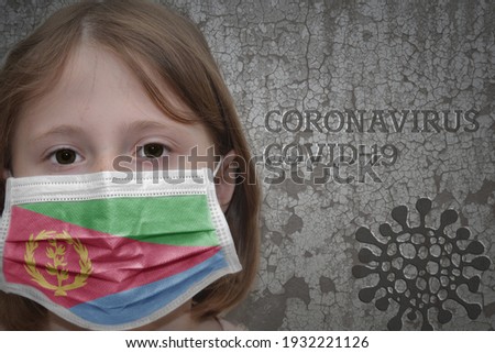 Little girl in medical mask with flag of eritrea stands near the old vintage wall with text coronavirus, covid, and virus picture. Stop virus