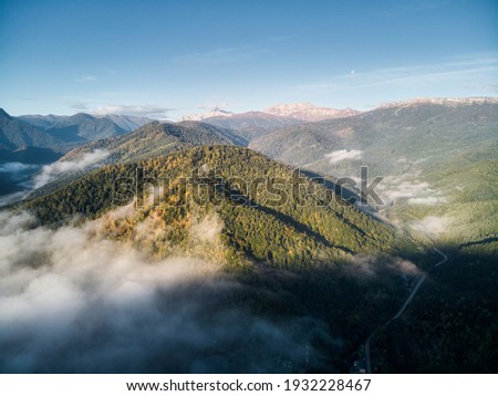 Aerial view, sea of fog and clouds on the background of the road to the mountains in autumn, illuminated by the rising sun. Russia