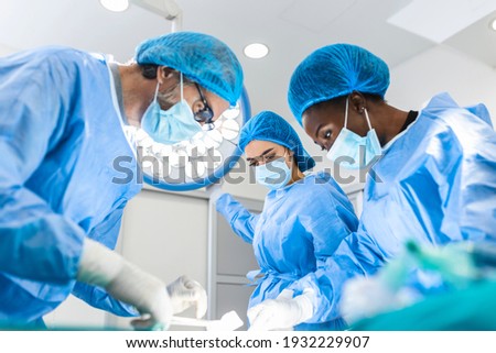 Preparation for the beginning of surgical operation with a cut. Group of surgeons at work in operating theater toned in blue. Medical team performing operation