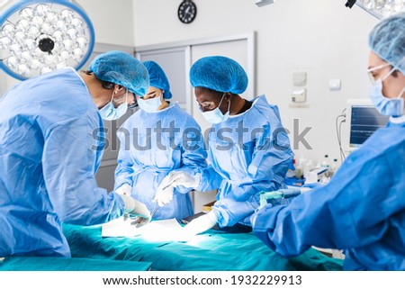 Surgical team performing surgery in modern operation theater,Team of doctors concentrating on a patient during a surgery,Team of doctors working together during a surgery in operating room, Royalty-Free Stock Photo #1932229913