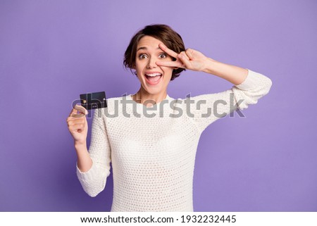 Photo portrait of pretty girl holding plastic showing v-sign gesture smiling isolated on pastel purple color background