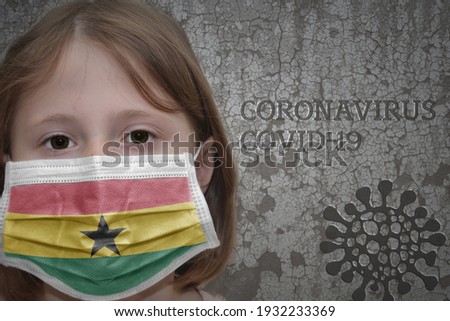 Little girl in medical mask with flag of ghana stands near the old vintage wall with text coronavirus, covid, and virus picture. Stop virus