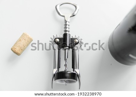 Metal corkscrew in a man's hand with a bottle of red wine on a background with a light white kitchen. Wine lover. Wine opener.