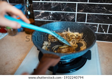 Close-up picture of female hand, stirring fried chopped onions on the pan, in the kitchen area.