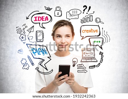 Portrait of young businesswoman in white shirt holding smart phone near concrete wall with diverse icons drawing. Concept of plans and strategy, ideas and online education
