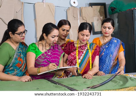Inspector holding clipboard explaining women textile worker sewing garment on production line Royalty-Free Stock Photo #1932243731