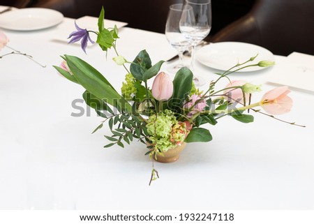 beautiful composition of pink tulips, wildflowers, with leaves, on a table with a white tablecloth, indoors, in a hotel, in the afternoon. Florist work, wedding decor, holidays. Profitable business,