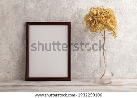 Brown wooden frame mockup with dried hydrangea in glass on gray concrete background. Blank, vertical orientation, still life, copy space.