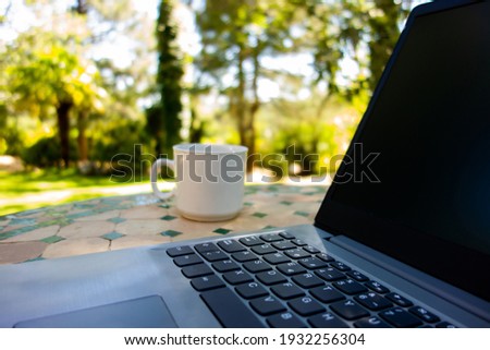 
Laptop on a mosaic table with a mug beside it, in a country house garden Royalty-Free Stock Photo #1932256304
