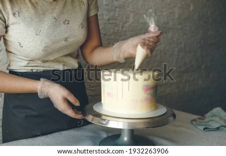 A pastry chef girl makes a wedding cake with her own hands and squeezes the cream on the layers of the cake. A pastry chef makes a pink cream using a cooking spatula.