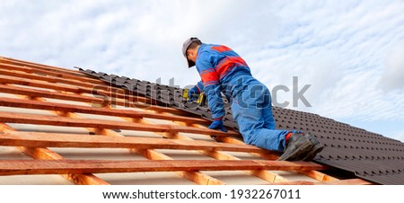 Man worker uses a power drill to attach a cap  metal roofing job with screws.