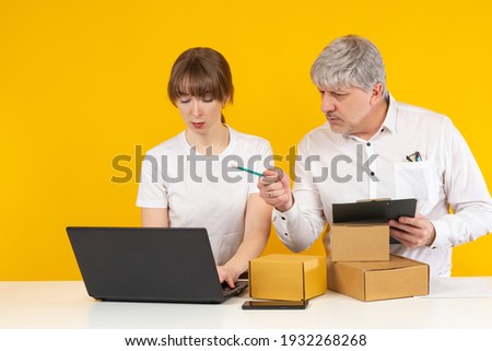 Businessman next to his assistant. Online store employees on a yellow background. Concept - man leads a secretary. Online store employees during work. Online store workers next to boxes.