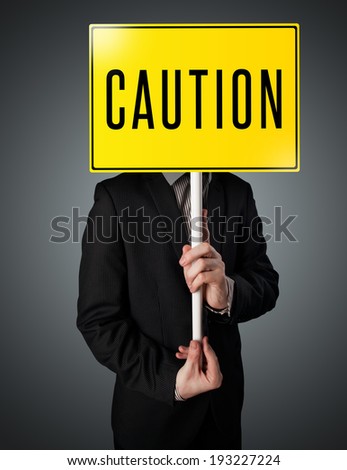 Businessman standing and holding a yellow caution sign in front of his head
