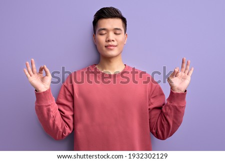 young asian male meditating, keep calm in yoga pose with eyes closed, chinese guy in casual wear posing at camera, enjoying time alone in silence.