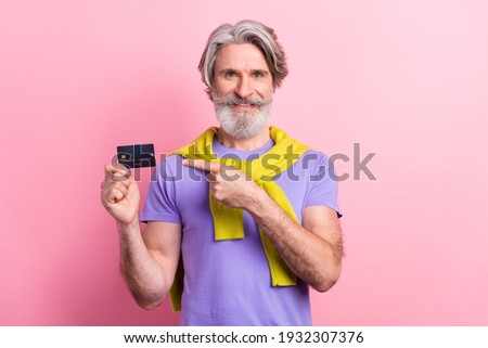 Portrait of handsome elderly cheerful gray-haired man demonstrating bank card isolated on pink pastel color background