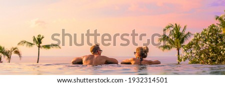 Panoramic photo of couple in pool enjoying tropical vacation by sunset