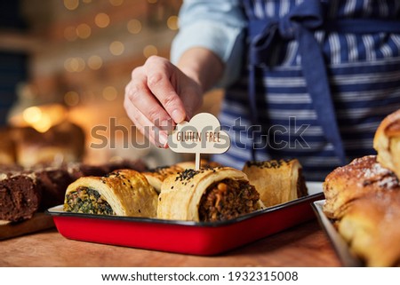 Sales Assistant In Bakery Putting Gluten Free Label Into Freshly Baked Savoury Roll Royalty-Free Stock Photo #1932315008
