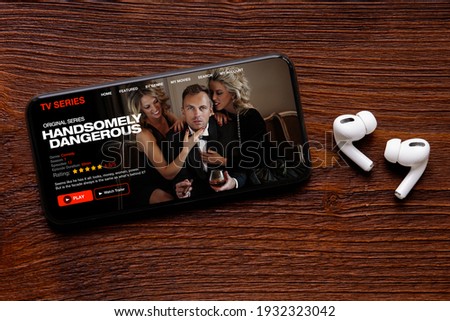 TV series and movies streaming app on mobile phone with wireless earbuds on table