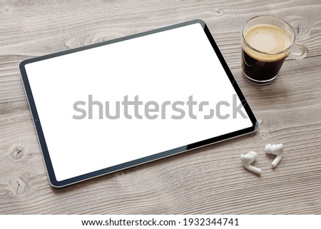 Tablet with blank white screen, wireless earphones and cup of coffee on wooden desk