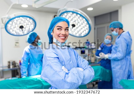 Close-up of a surgeon woman looking at camera with colleagues performing in background in operation room. The concept of medicine