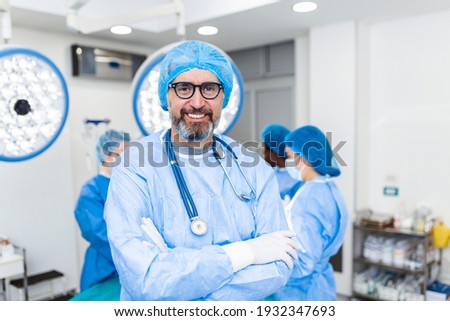 Portrait of male surgeon standing with arms crossed in operation theater at hospital. Team surgeons are performing an operation, middle aged doctor is looking at camera, in a modern operating room Royalty-Free Stock Photo #1932347693