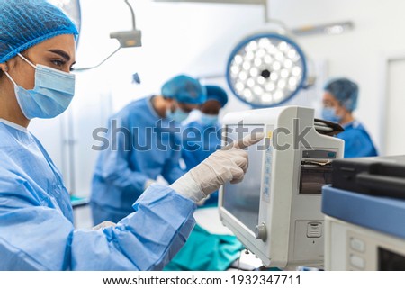 Diverse Team of Professional Surgeons Performing Invasive Surgery on a Patient in the Hospital Operating Room. Nurse Hands Out Instruments to surgeon, Anesthesiologist Monitors Vitals.