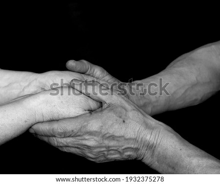 A black and white photo of an adult man and woman holding hands on a black background. Concept together forever. Elderly man and woman. Elderly couple holding hands