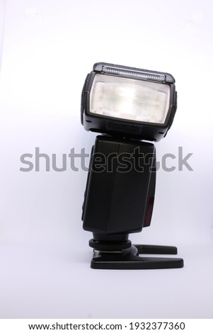 One black portable external flash in profile with the head turned to the side against a light background