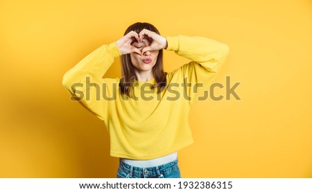 Happy brunette woman making heart symbol with hands posing isolated on bright yellow background
