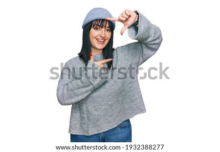 Young hispanic woman wearing cute wool cap smiling making frame with hands and fingers with happy face. creativity and photography concept. 