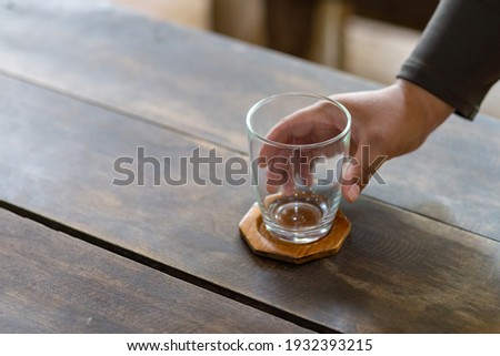 A clear glass and wooden coaster are placed on a wooden table and a handle.
