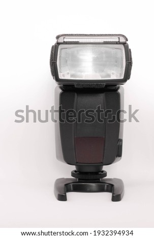 One medium portable black plastic external flash unit in front on a light background close up