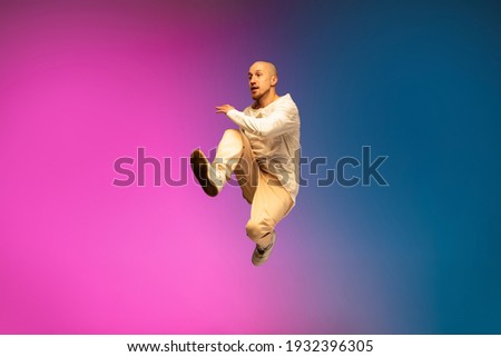 Flying high. Stylish sportive caucasian man dancing hip-hop on colorful gradient background at dance hall in neon light. Youth culture, movement, style and fashion, action. Fashionable bright portrait